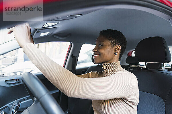 Glückliche junge Frau stellt den Rückspiegel im Auto ein