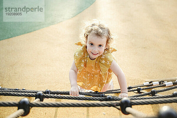 Smiling girl climbing on rope at jungle gym