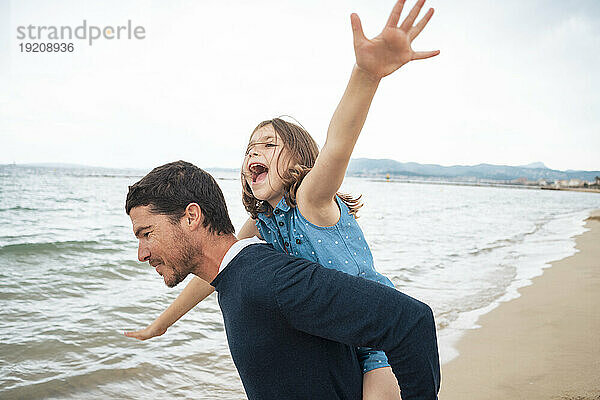 Glücklicher Vater gibt Huckepackfahrt und hat Spaß mit Tochter am Strand