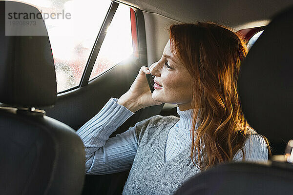 Glückliche rothaarige Frau  die im Auto mit dem Smartphone spricht