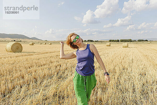 Lächelnde Frau mit Sonnenbrille spaziert im Weizenfeld