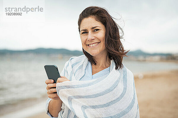 Glückliche Frau steht mit Smartphone am Strand