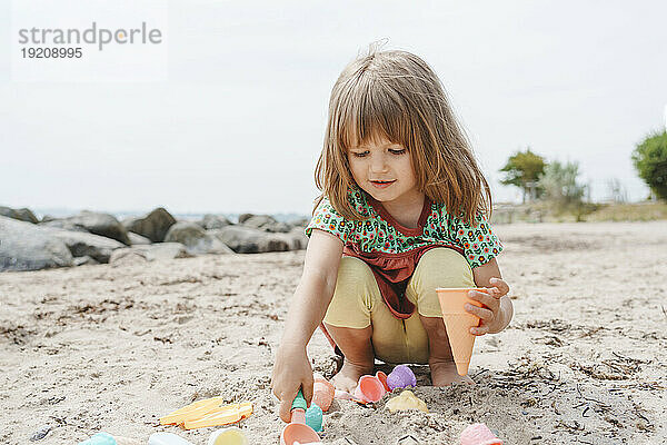 Mädchen spielt im Sand mit Zapfen am Strand