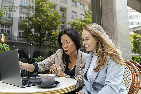 Geschäftsfrau zeigt ihrem Partner im Straßencafé ihren Laptop
