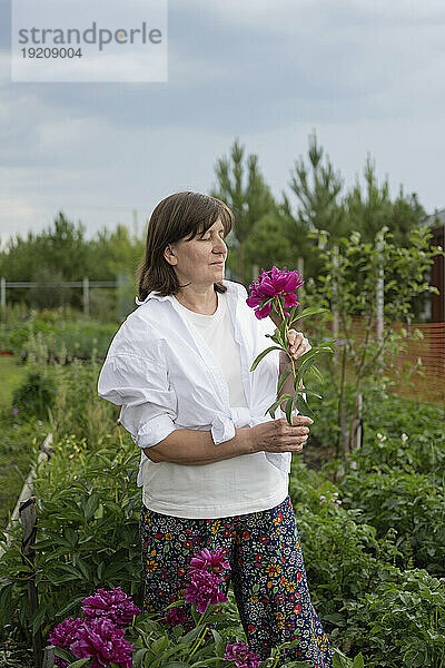 Reife Frau riecht Blumen im Garten