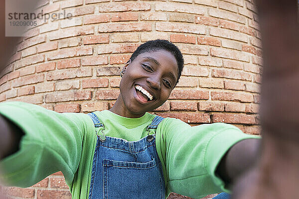 Happy young woman taking selfie in front of brick wall