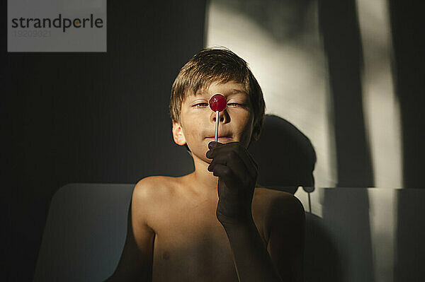 Boy holding red lollipop at home