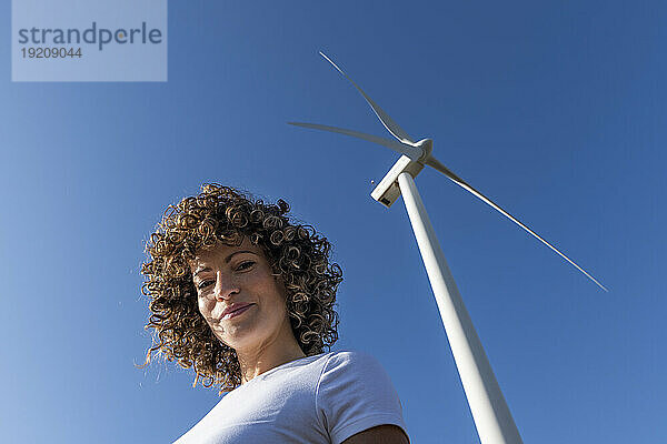 Lächelnde Frau vor der Windkraftanlage an einem sonnigen Tag