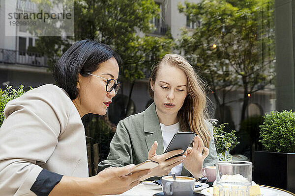 Geschäftsfrau zeigt ihrem Partner im Straßencafé ihr Smartphone