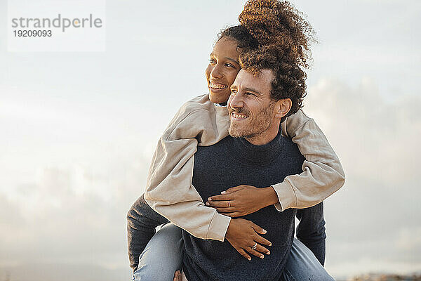 Happy man giving piggyback ride to girlfriend at beach
