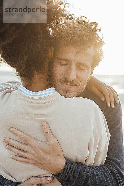 Mann mit geschlossenen Augen umarmt Freundin am Strand