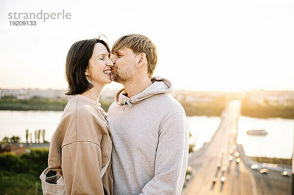 Glücklicher Mann küsst Frau an sonnigem Tag am Flussufer