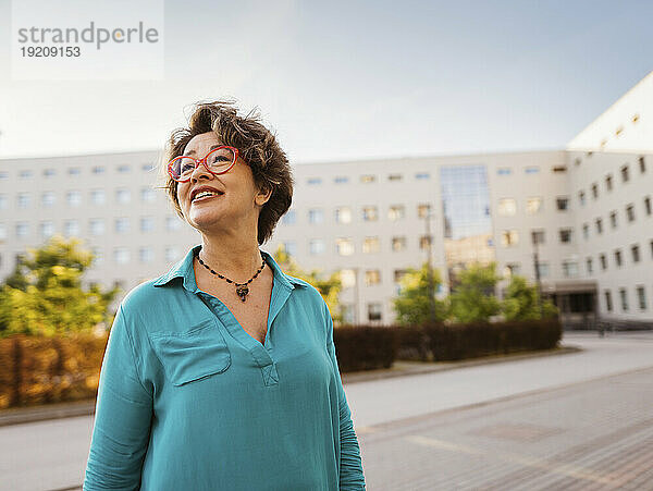 Lächelnde Geschäftsfrau  die vor dem Bürogebäude nachdenkt
