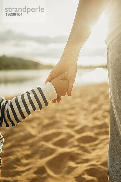 Mutter und Sohn halten Händchen am Strand