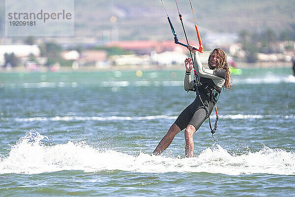 Fröhlicher Sportler beim Kitesurfen im Meer an einem sonnigen Tag