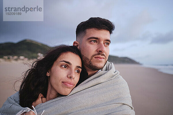 Nachdenkliches Paar in Decke gehüllt am Strand