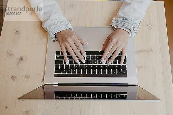 Hände einer Frau  die am Schreibtisch auf dem Laptop tippt