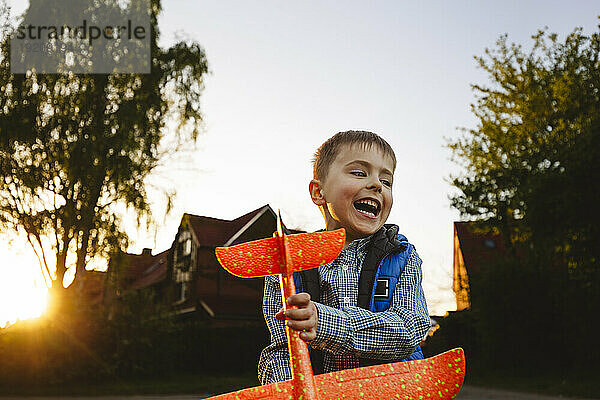 Lächelnder Junge hält Spielzeugflugzeug bei Sonnenuntergang