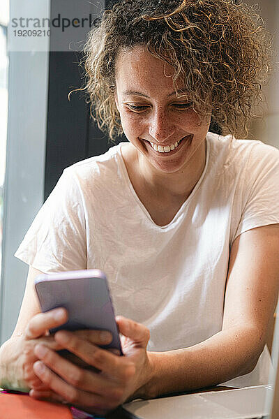 Lächelnde Geschäftsfrau benutzt Mobiltelefon im Café