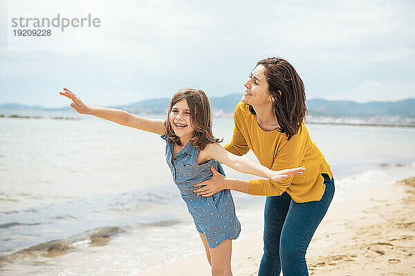 Fröhliche Mutter spielt mit Tochter am Strand