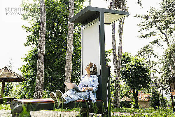 Frau sitzt mit Laptop in der Nähe einer Solarladestation im Park