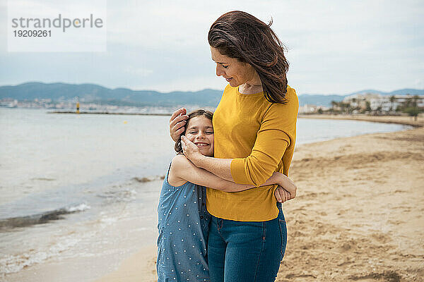Lächelndes Mädchen umarmt Mutter am Strand