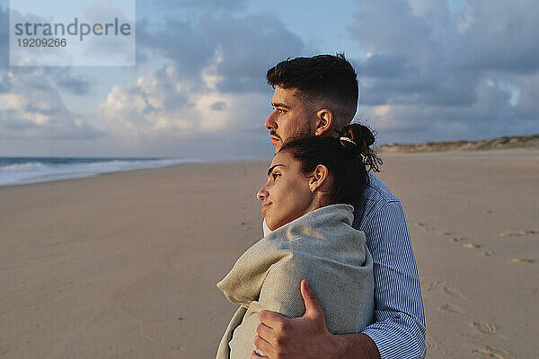 Mann umarmt Freundin am Strand