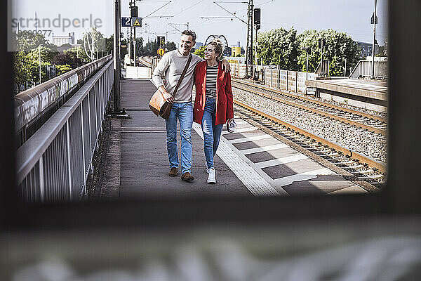 Glückliches Paar  das an einem sonnigen Tag gemeinsam am Bahnsteig spaziert