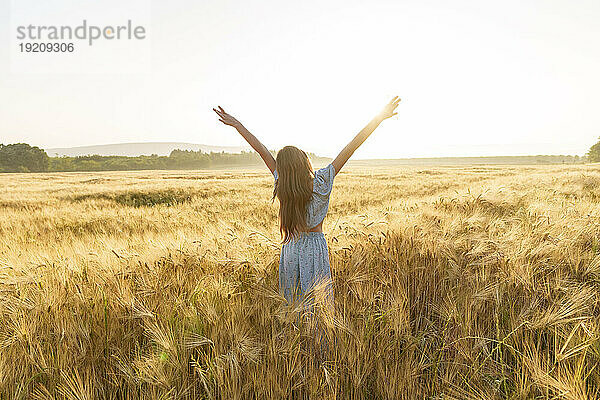 Mädchen mit langen Haaren streckt die Arme inmitten der Weizenernte im Feld aus