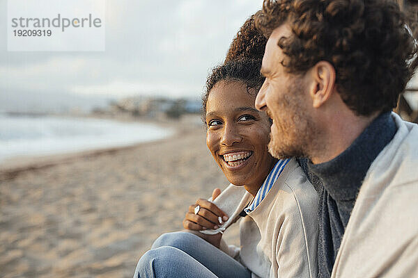 Cheerful couple spending leisure time sitting at beach