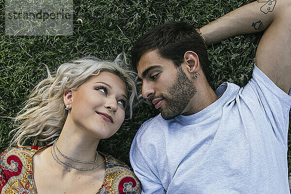 Young couple staring at each other lying on grass