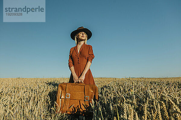 Lächelnde Frau mit Koffer im Weizenfeld