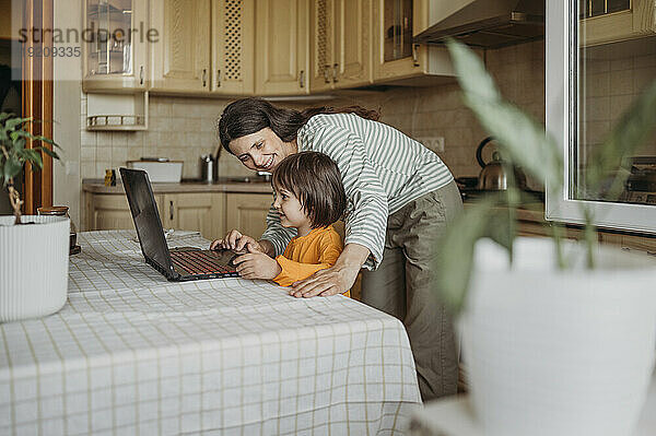 Mutter hilft Sohn dabei  Online-Unterricht auf dem Laptop am Esstisch anzusehen