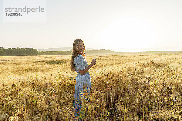 Lächelndes Mädchen mit langen Haaren  das inmitten der Weizenernte auf dem Feld steht