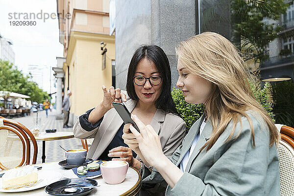 Geschäftsfrau zeigt ihrem Partner ihr Smartphone im Straßencafé