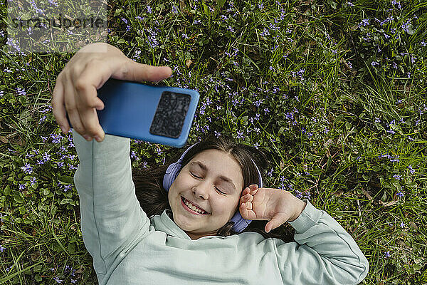 Lächelndes Mädchen macht ein Selfie mit dem Smartphone  das im Gras liegt