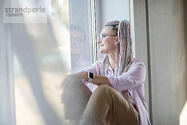 Nachdenkliche Frau sitzt zu Hause am Fenster