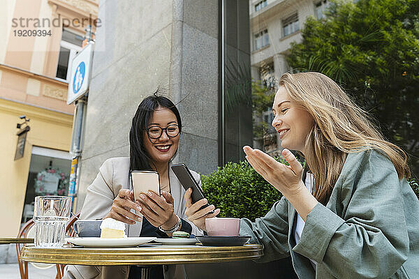 Lächelnde Geschäftspartner nutzen Smartphones und sitzen im Straßencafé