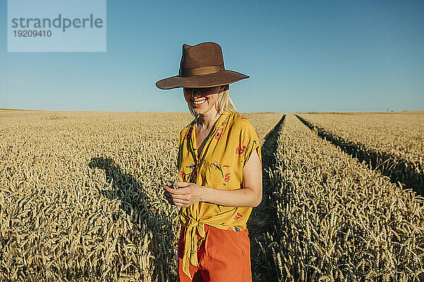 Lächelnde Frau mit Hut steht im Weizenfeld