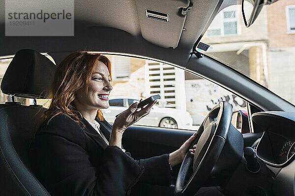 Glückliche Geschäftsfrau  die im Auto mit dem Smartphone spricht