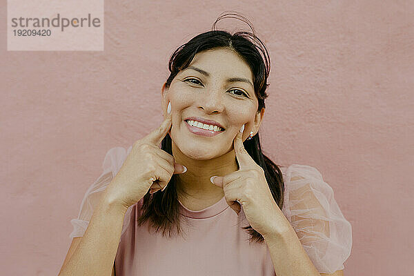 Glückliche Frau berührt Gesicht vor rosa Wand