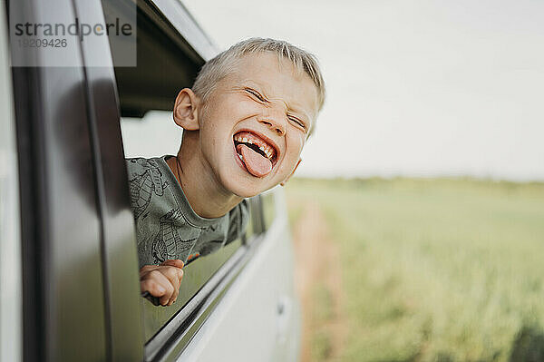 Lächelnder Junge mit herausgestreckter Zunge  der aus dem Autofenster schaut