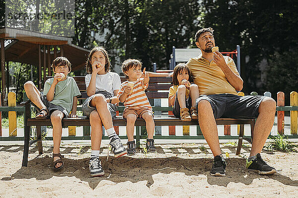 Nachdenklicher Vater mit Söhnen beim Eisessen auf einer Parkbank