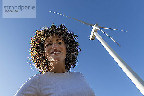 Glückliche Frau vor der Windkraftanlage an einem sonnigen Tag