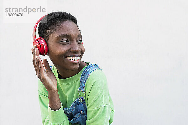 Glückliche junge Frau mit kabellosen Kopfhörern vor weißer Wand