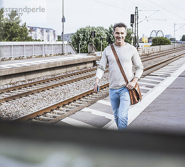 Glücklicher Mann mit Umhängetasche  der am Bahnhof läuft