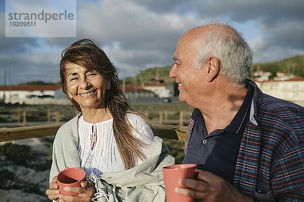 Glückliche ältere Frau und Mann halten Kaffeetassen unter bewölktem Himmel