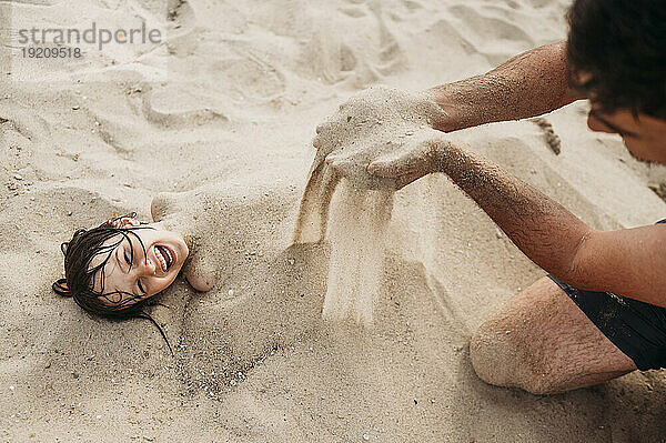Father covering son with sand and having fun together