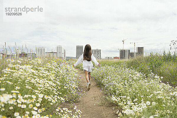 Sorgloses Mädchen rennt inmitten von Gänseblümchen auf der Wiese