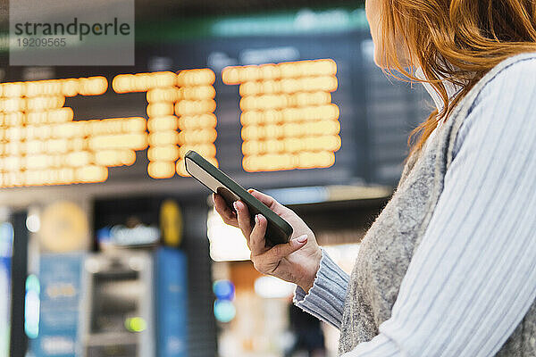 Frau mit Smartphone schaut auf die Ankunfts- und Abflugtafel